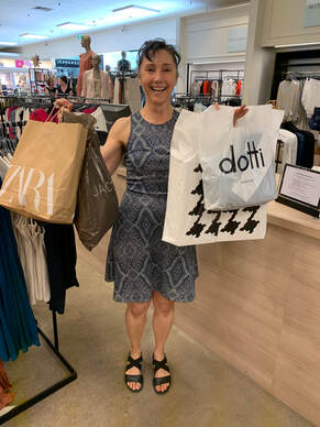 The Perth Fashion Stylist client Claire standing in shop holding bags of new clothes up and smiling