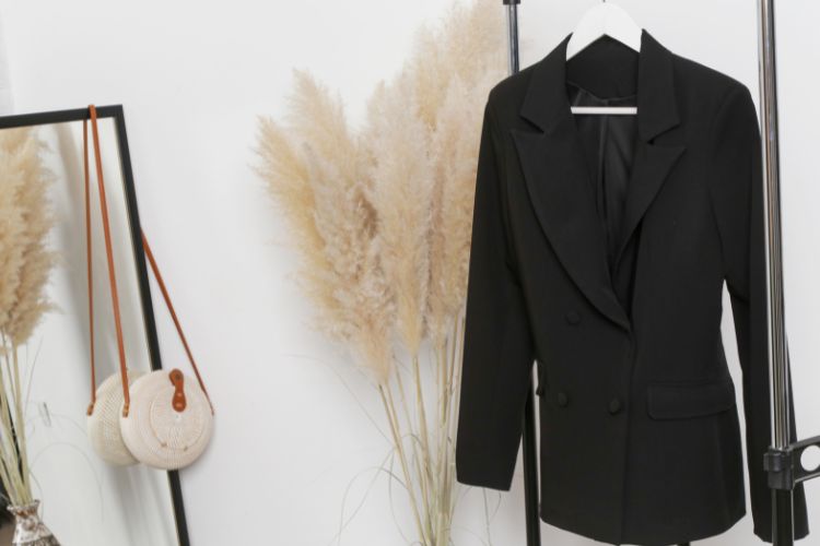 Black blazer hanging on clothes hanger in room besides mirror